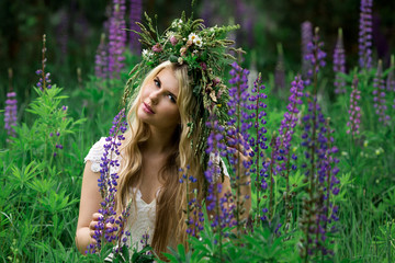 Beautiful girl in white dress in lupine field