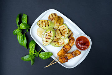 grilled tofu kebab on a white plate. Black background. Fresh basil leaves.