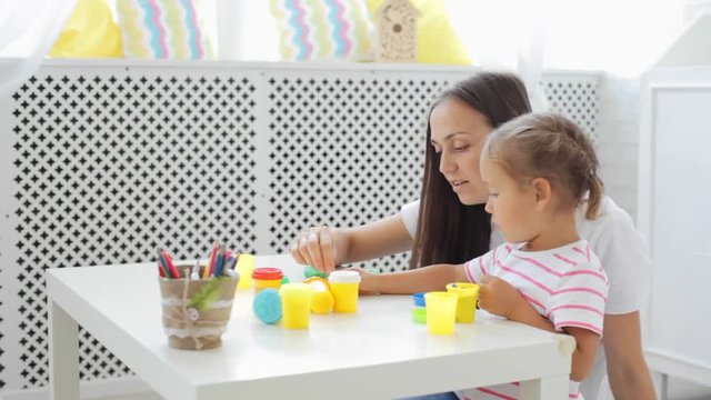 Mother with cute little daughter play with modeling clay at light living room.