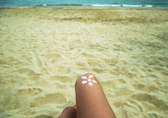 Legs of a girl lying on a beach deckchair by the sea. The sun, painted on sunburnt skin of the foot with sunscreen.