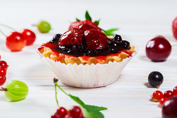 Delicious fruit cake on white wooden background with strawberries, cherries, currants and raspberries. Beautiful, delightful and healthy desserts