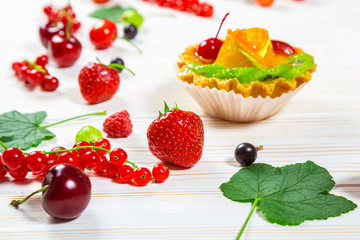Delicious fruit cake on white wooden background with strawberries, cherries, currants and raspberries. Beautiful, delightful and healthy desserts
