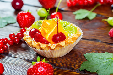 Delicious fruit cake on brown wooden background with strawberries, cherries, currants and raspberries. Beautiful, delightful and healthy desserts