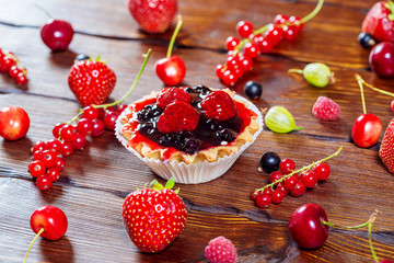 Delicious fruit cake on brown wooden background with strawberries, cherries, currants and raspberries. Beautiful, delightful and healthy desserts