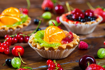Delicious fruit cake on brown wooden background with strawberries, cherries, currants and raspberries. Beautiful, delightful and healthy desserts
