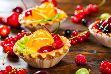 Delicious fruit cake on brown wooden background with strawberries, cherries, currants and raspberries. Beautiful, delightful and healthy desserts