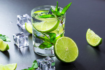 Mojito cocktail with lime, ice cubes and mint in highball glass on a black background Copy space