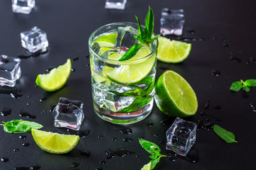 Mojito cocktail with lime, ice cubes and mint in highball glass on a black background Copy space