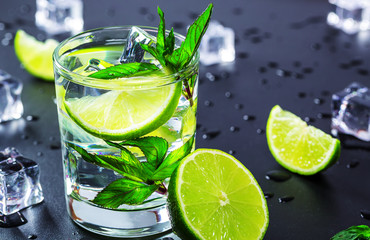 Mojito cocktail with lime, ice cubes and mint in highball glass on a black background Copy space