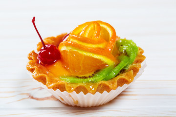 A delicious fruit dessert in a waffle tartlets with sweet cream, orange, kiwi and cherry on white wooden table. Beautiful, delicious and healthy cake background