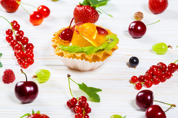 Delicious fruit cake on white wooden background with strawberries, cherries, currants and raspberries. Beautiful, delightful and healthy desserts