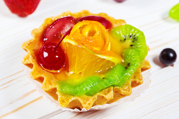 A delicious fruit dessert in a waffle tartlets with sweet cream, orange, kiwi and cherry on white wooden table. Beautiful, delicious and healthy cake background