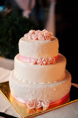 White wedding cake decorated with roses, standing on golden plate