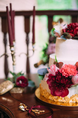 Wedding cake decorated with red, pink peony flowers, standing on golden plate with two golden spoon