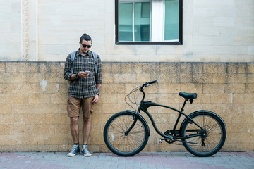 Fototapeta premium Handsome Young Man Cyclist Standing Next To Bike And His Looking At Smartphone. Street Lifestyle Urban Everyday Concept