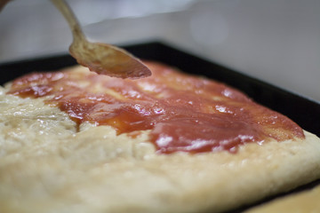 Preparing a pizza with tomatoes sauce before baking.