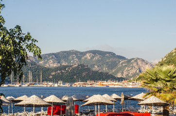 Summer panorama of the beach at sea and high mountains against the background of yachts and ships. Canal at sea.
