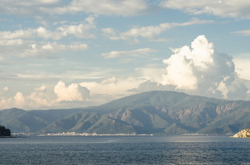 Summer panorama of the beach at sea and high mountains against the background of yachts and ships. Island in the middle of the sea. Ocean and islands