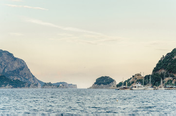 Summer panorama of the beach at sea and high mountains against the background of yachts and ships. Island in the middle of the sea. Ocean and islands