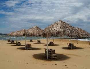 Straw umbrellas and beach furniture in a beautiful sandy beach under a  blue sky with many clouds