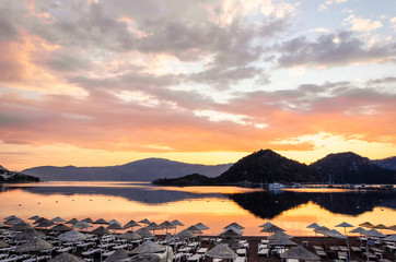 Colorful sunset on the beach against the background of the sea and the mountains. Rest on the sea. Beach umbrellas and skiers.