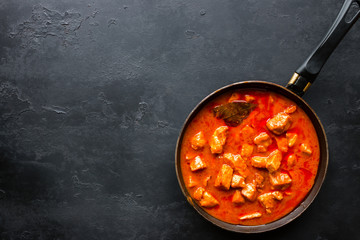 Frying pan with stewed meat on a black background and space for text
