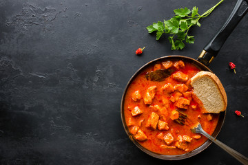 Frying pan with braised meat in spices and parsley on a black background