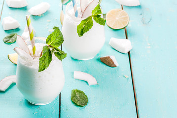 Summer refreshment drinks, cocktails. Frozen coconut mojito with lime and mint. Pina colada. On a light blue green wooden table with ingredients. Copy space - obrazy, fototapety, plakaty