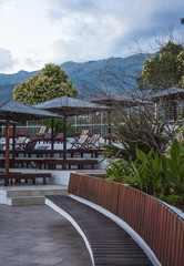 Bench. Pool umbrella.  Outdoor wooden benches  stools beside the swimming pool near the garden  at the resort hotel. View of the mountains.