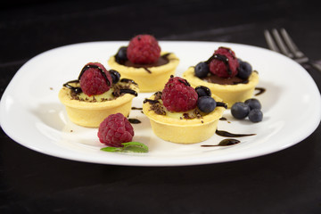 A delicious dessert with vanilla and chocolate pudding  in a basket on the white plate with fresh raspberries and blueberries. Light summer sweets