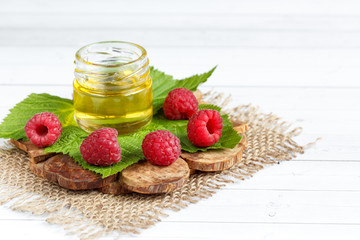 The bowl with honey, berries and leaves of raspberry on a wooden stand. Spoon with honey