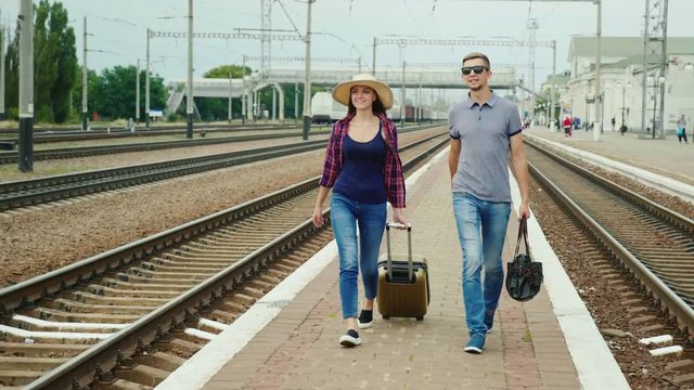 Young happy couple of tourists with travel bags go along the peron along the railroad. Beginning a great journey. Steadicam shot