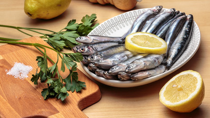 Oval dish with raw anchovies, beside parsley, salt and lemons. Mediterranean diet