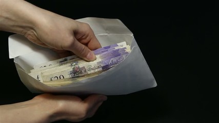 Close-up man's hand giving envelope with money to woman's hand. Black background. The transfer of cash from hand to hand. Female hands open an envelope and counting a lot of 20 pounds (GBP) banknotes.