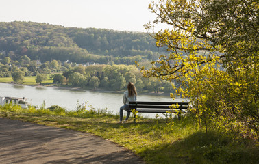 Young woman sitting on a bench for rest among trees on the shore of a river. Park. Landscape.   