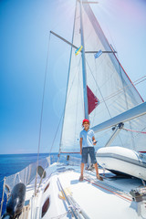 Fototapeta premium Little boy captain on board of sailing yacht on summer cruise. Travel adventure, yachting with child on family vacation.
