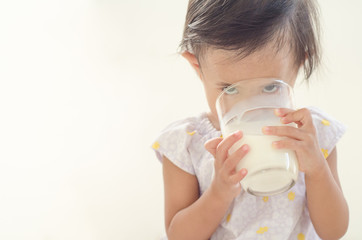 Cute asian toddler girl drinking milk from big glass on white background.