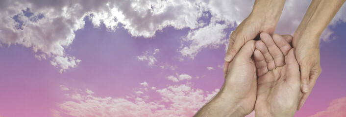 Caring in the Community Charity banner -  wide banner with a woman's hands holding a man's cupped hands in a needy gesture on a beautiful pink and blue sky background  with copy space on the left
