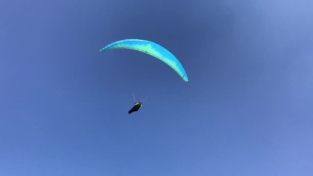 t&uuml;rkisfarbener Paragleiter / Gleitschirm kreist im blauen Himmel durch die L&uuml;fte