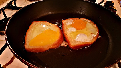 Eggs are roasted inside a slice of white bread in oil in a frying pan
