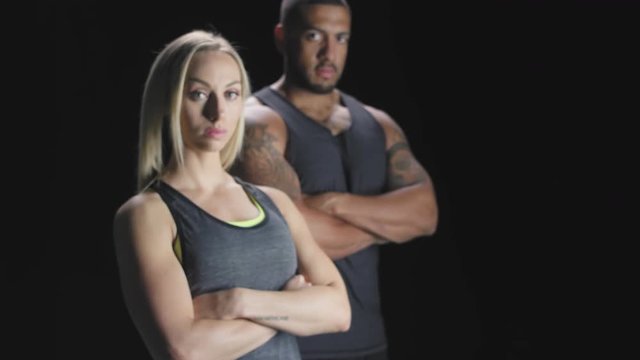 Zooming portrait shot of an athletic man and woman with their arms crossed on a dark background