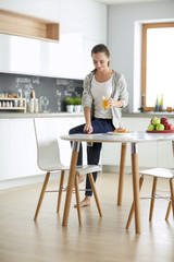 Young woman with orange juice and tablet in kitchen.