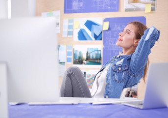 Two young woman standing near desk with instruments, plan and laptop.