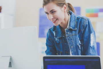 Young woman standing near desk with instruments, plan and laptop.