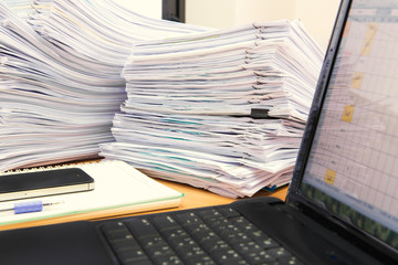 computer notebook and documents on desk stack up high waiting to be managed