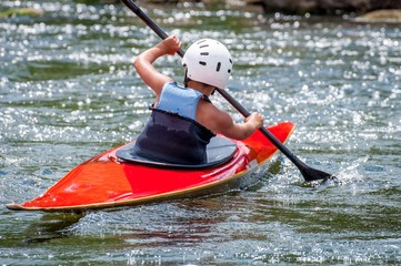 A teenager trains in the art of kayaking. Slalom boats on rough river rapids. The child is skillfully engaged in rafting.