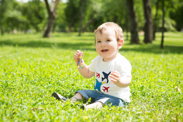 Summer portrait of beautiful baby boy sitting in the green grass