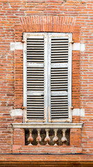 Vintage rustic ventilated closed wooden window shutters in brick house