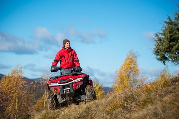 Naklejka premium Bottom view. A man on the red ATV quad bike against blue sky in the autumn landscape nature. Copy space