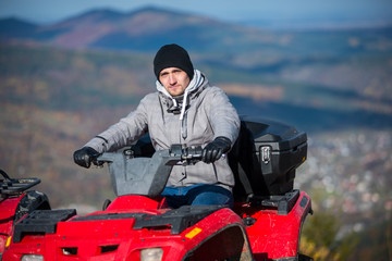 Close-up of man in winter clothing on red quad bike looking at the camera on the blurred background at sunny day